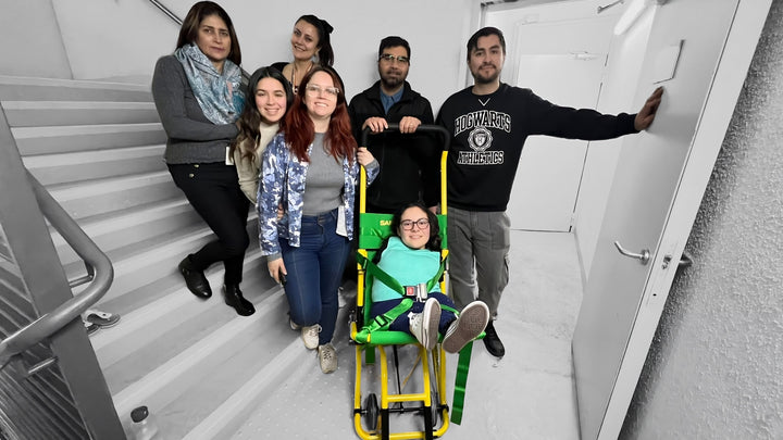 7 personas en un curso de capacitación de silla de evacuación, una de ellas sentada en la silla, 