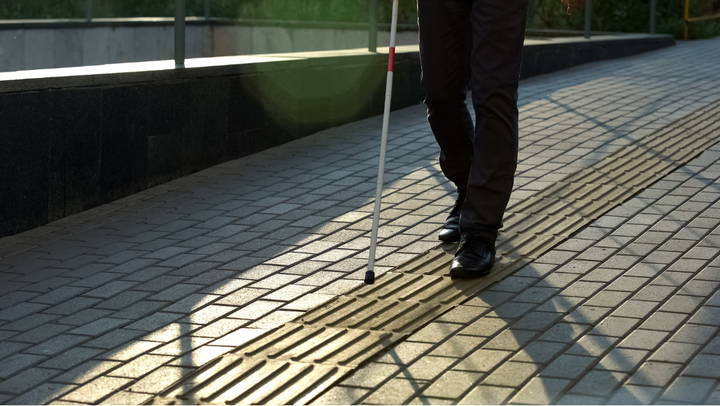 Persona con discapacidad visual usa un bastón blanco mientras camina sobre una huella podotáctil.