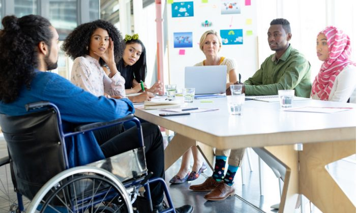 Grupo de personas alrededor de una mesa en una reunión de trabajo, con un participante en silla de ruedas.