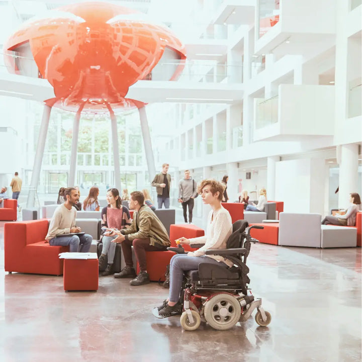 Personas conversando en espacio público accesible, con inclusión de usuario en silla de ruedas eléctrica.