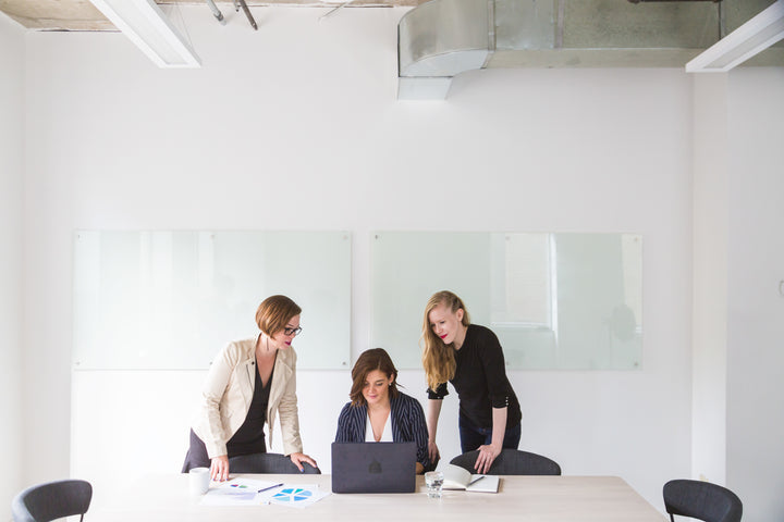 3 mujeres en una oficina mirando un computador. 